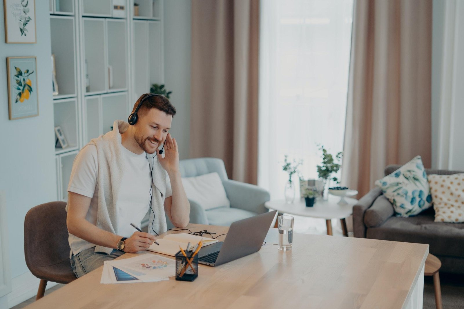 Happy guy making notes in notebook during online lesson at home